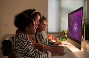 A woman uses the mouse on the 27-inch iMac while two children watch the screen.  